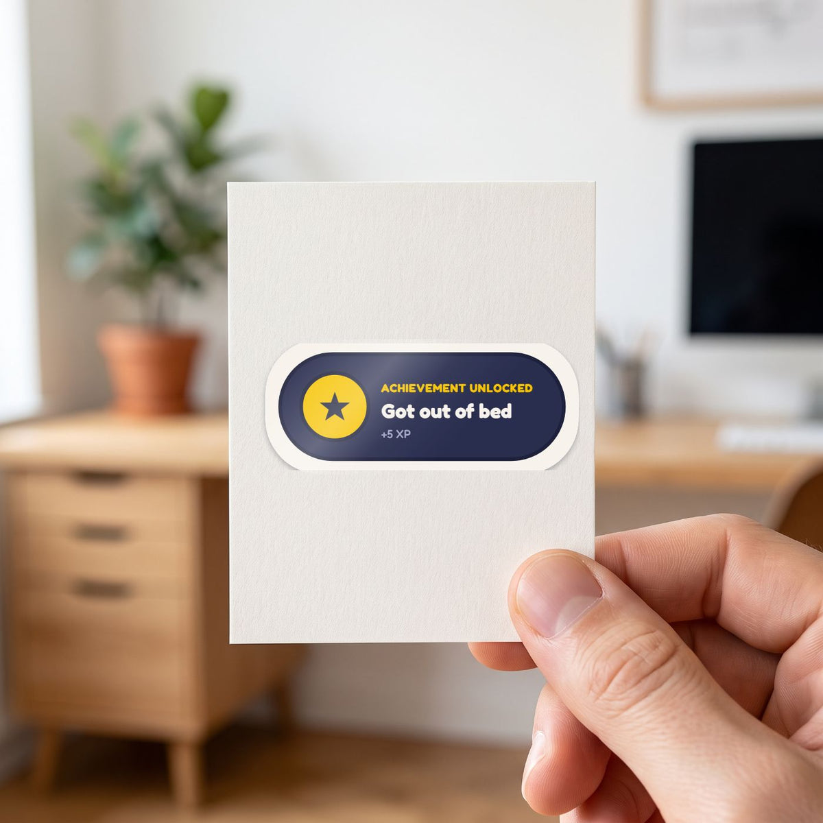 Achievement Unlocked: Got Out of Bed sticker held in a hand on its white backing card