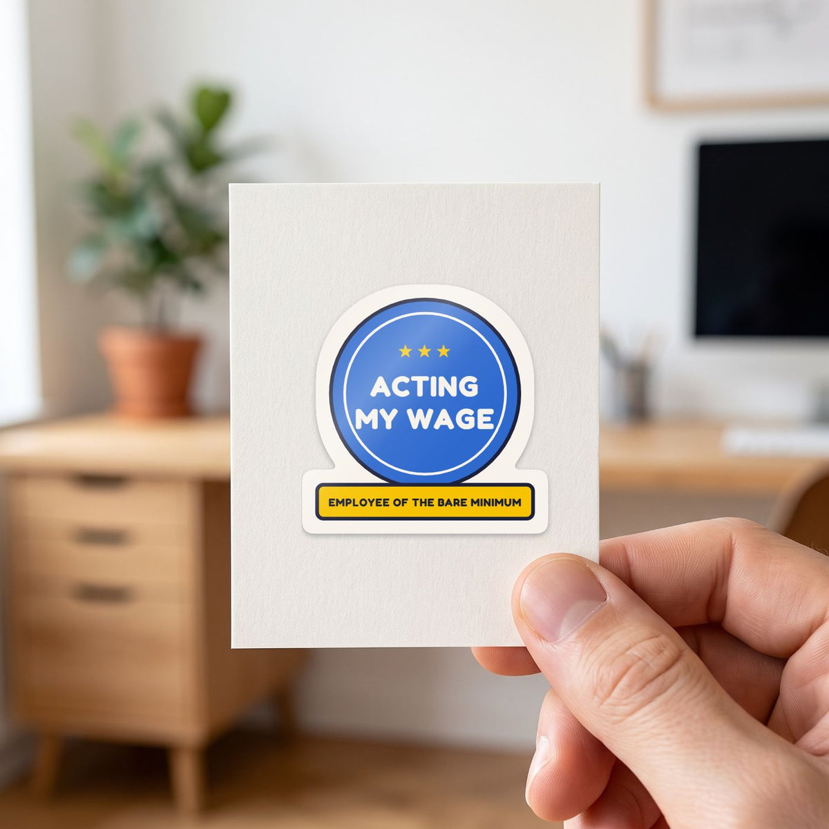Acting My Wage sticker held in a hand on its white backing card