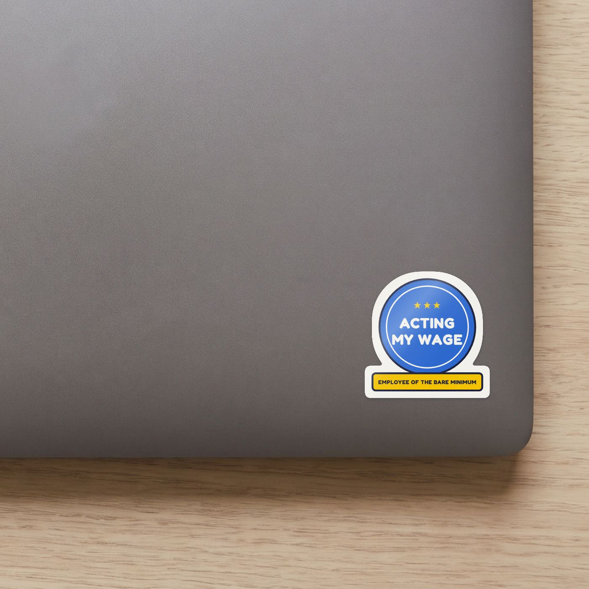 Acting My Wage sticker on the lid of a grey laptop