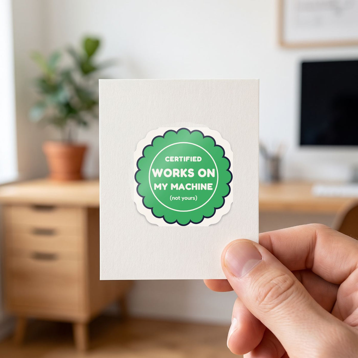 Certified: Works on My Machine sticker held in a hand on its white backing card