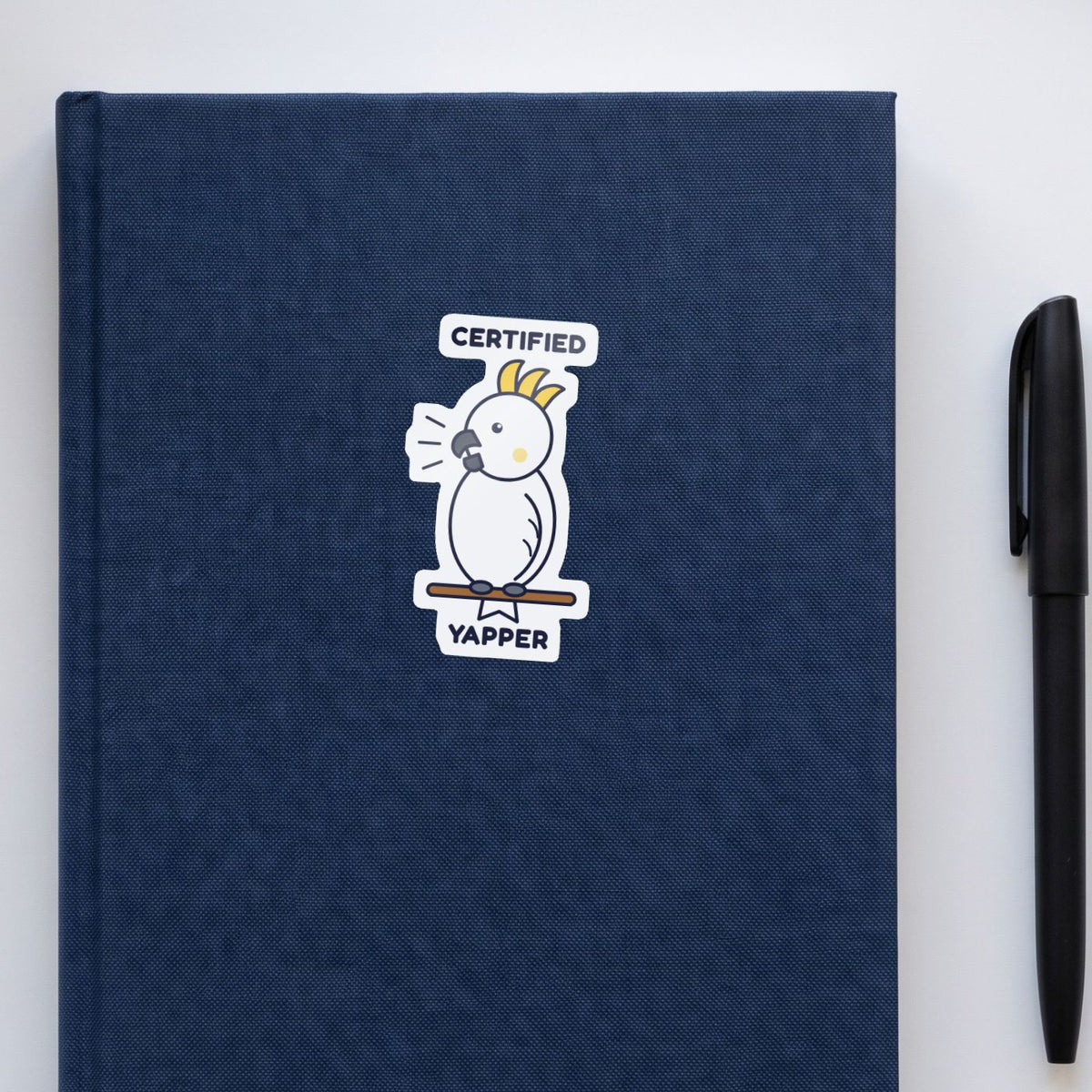 Certified Yapper sticker on a navy notebook