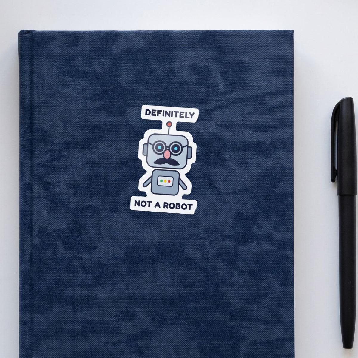 Definitely Not a Robot sticker on a navy notebook