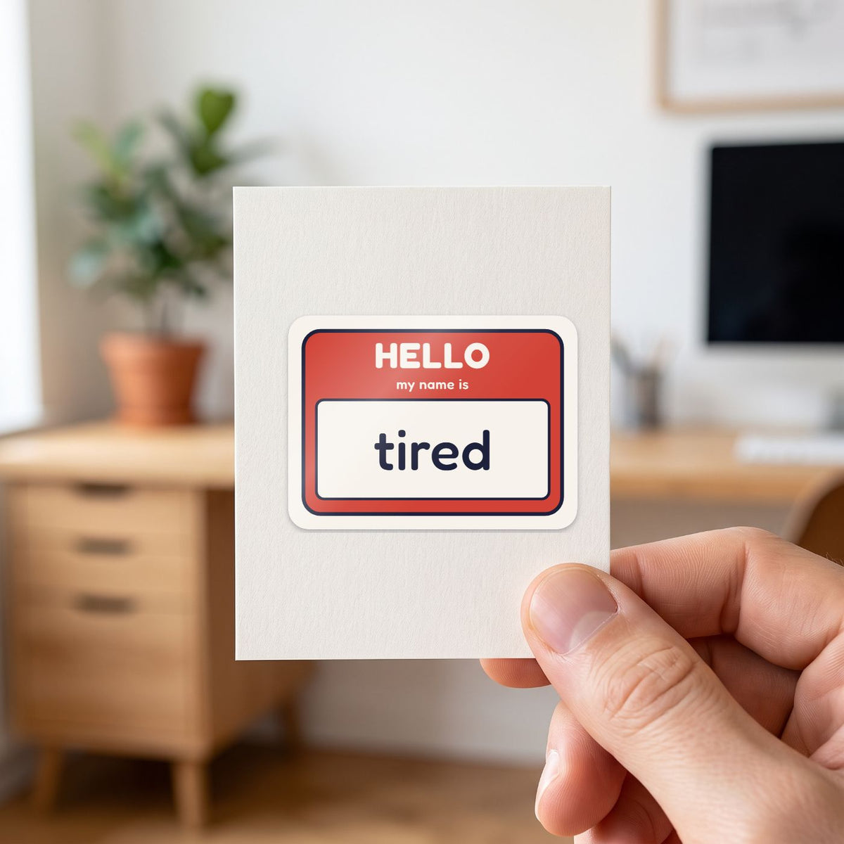 Hello, My Name Is Tired sticker held in a hand on its white backing card