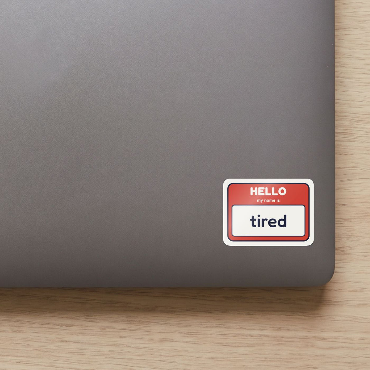 Hello, My Name Is Tired sticker on the lid of a grey laptop