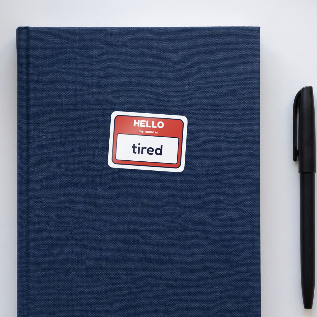 Hello, My Name Is Tired sticker on a navy notebook