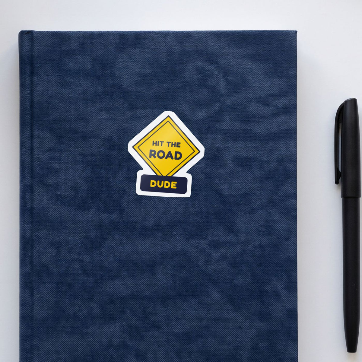 Hit the Road, Dude (Road Sign) sticker on a navy notebook