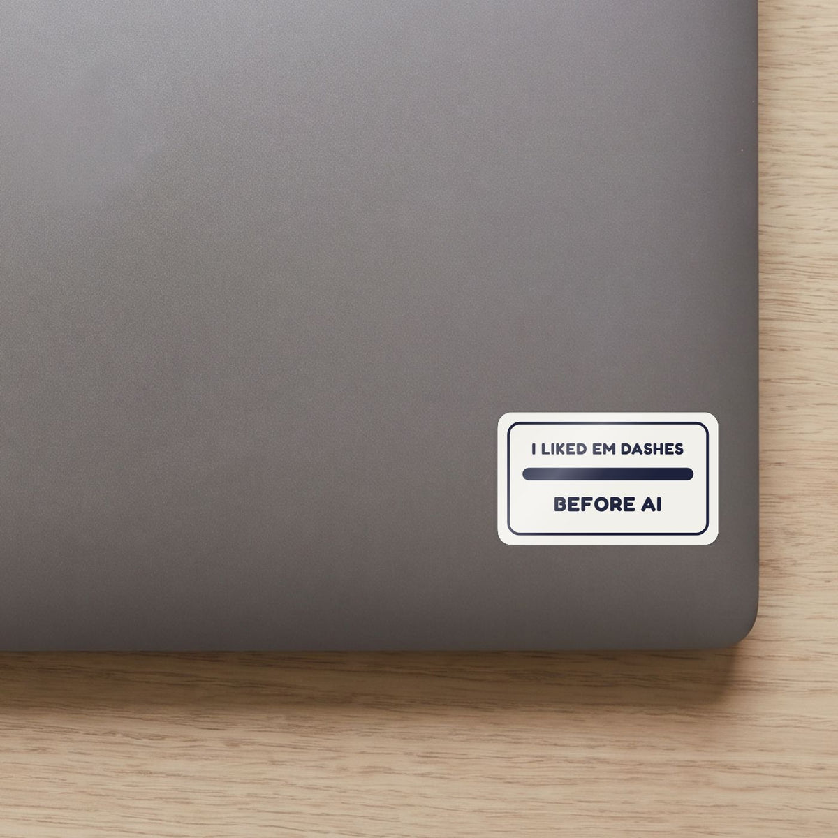 I Liked Em Dashes Before AI sticker on the lid of a grey laptop