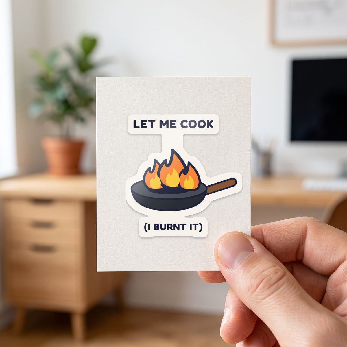 Let Me Cook sticker held in a hand on its white backing card