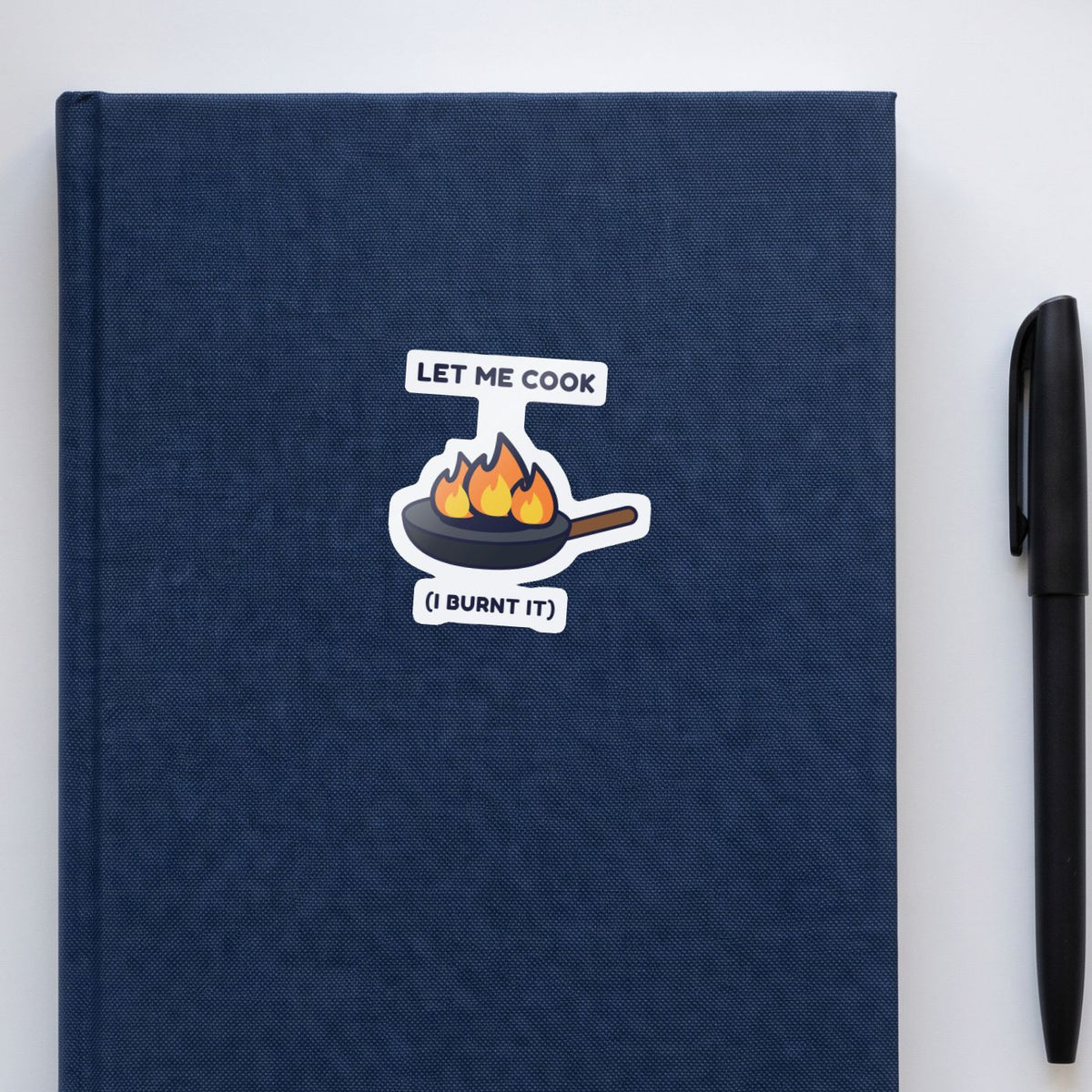 Let Me Cook sticker on a navy notebook