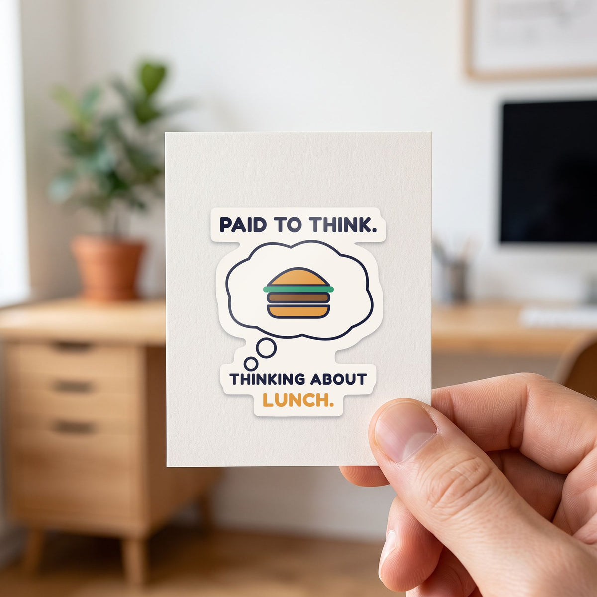 Paid to Think. Thinking About Lunch. sticker held in a hand on its white backing card