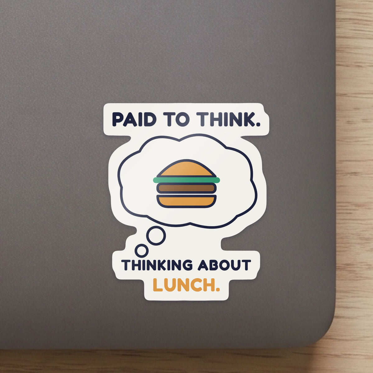 Paid to Think. Thinking About Lunch. sticker close up on a laptop lid, showing the gloss and the white cut edge