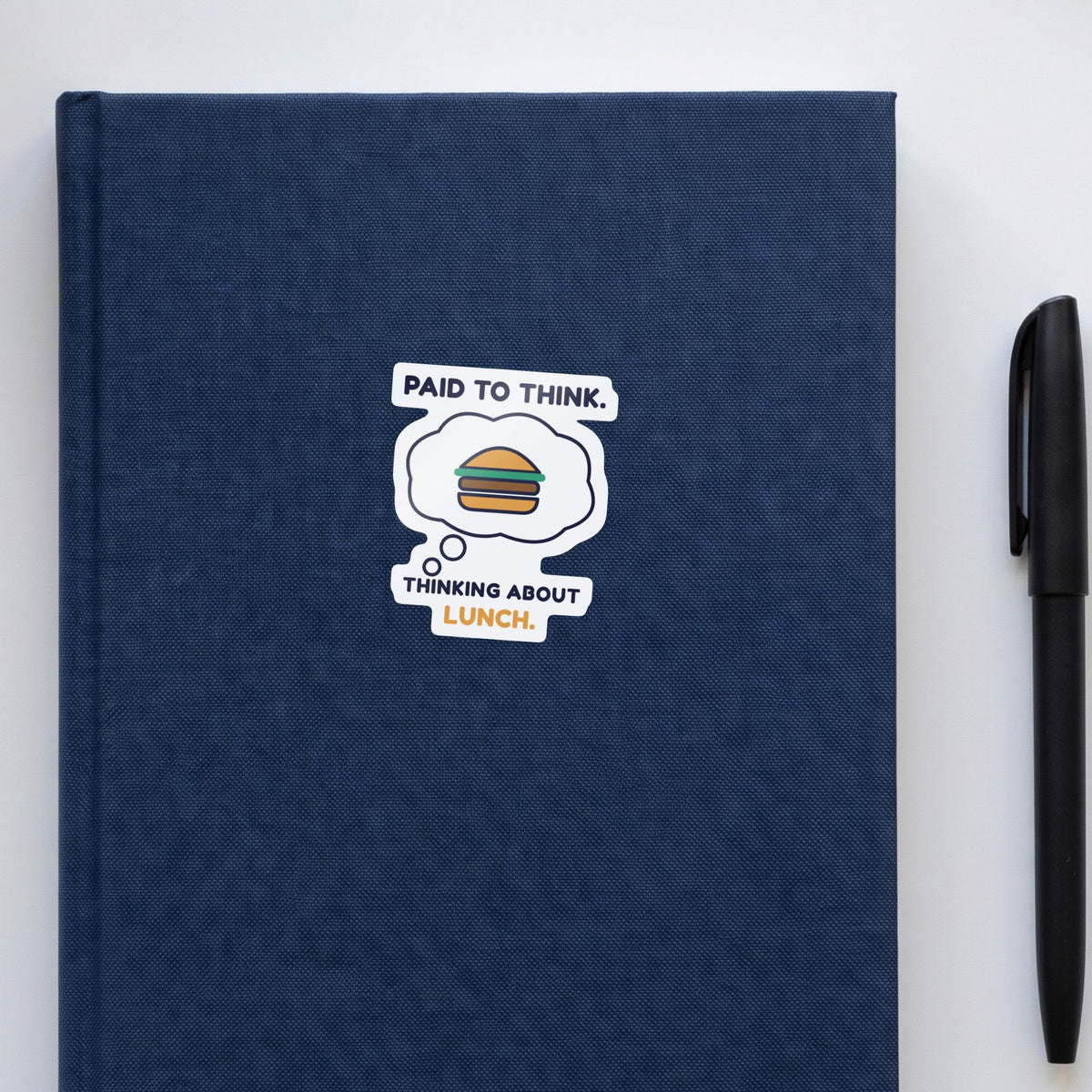 Paid to Think. Thinking About Lunch. sticker on a navy notebook