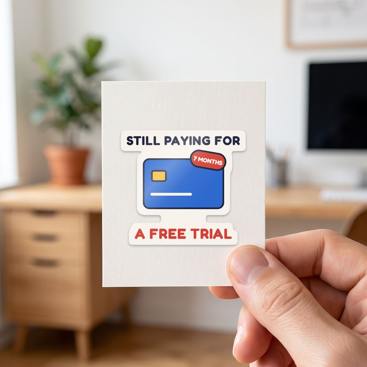 Still Paying for a Free Trial sticker held in a hand on its white backing card
