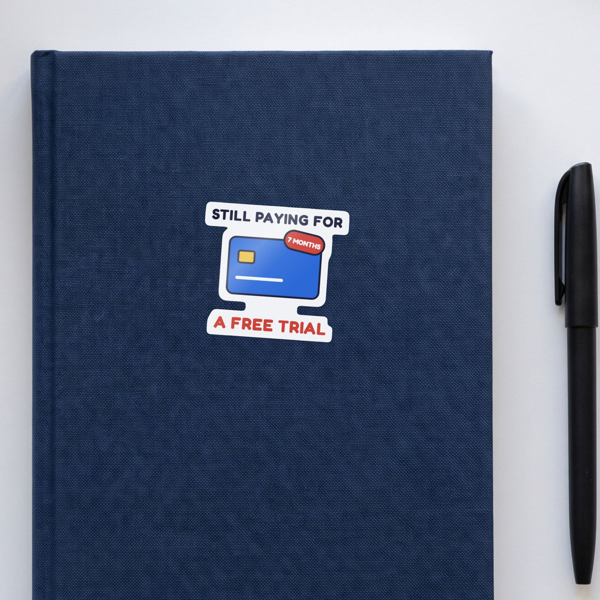 Still Paying for a Free Trial sticker on a navy notebook