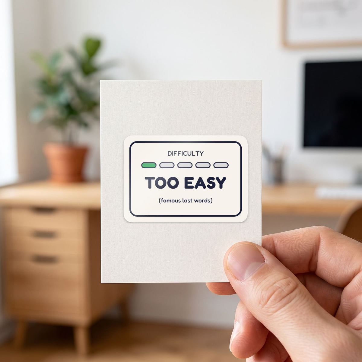 Too Easy sticker held in a hand on its white backing card