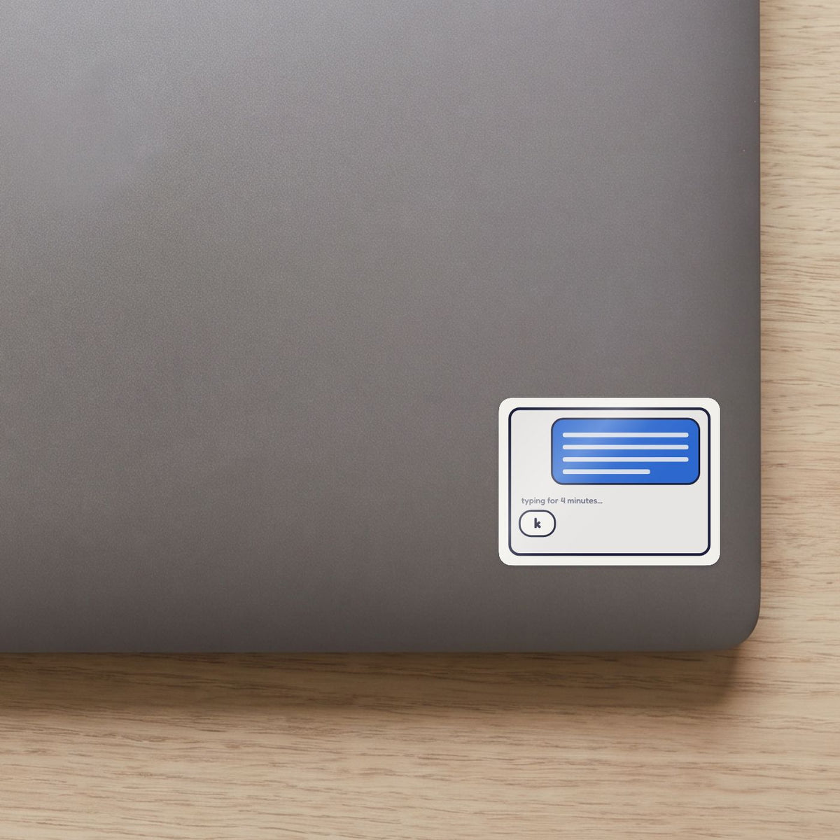 Typing for 4 Minutes: k sticker on the lid of a grey laptop